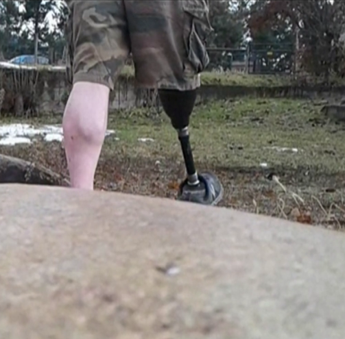 The lower body of a man with a prosthetic leg marching away from the camera