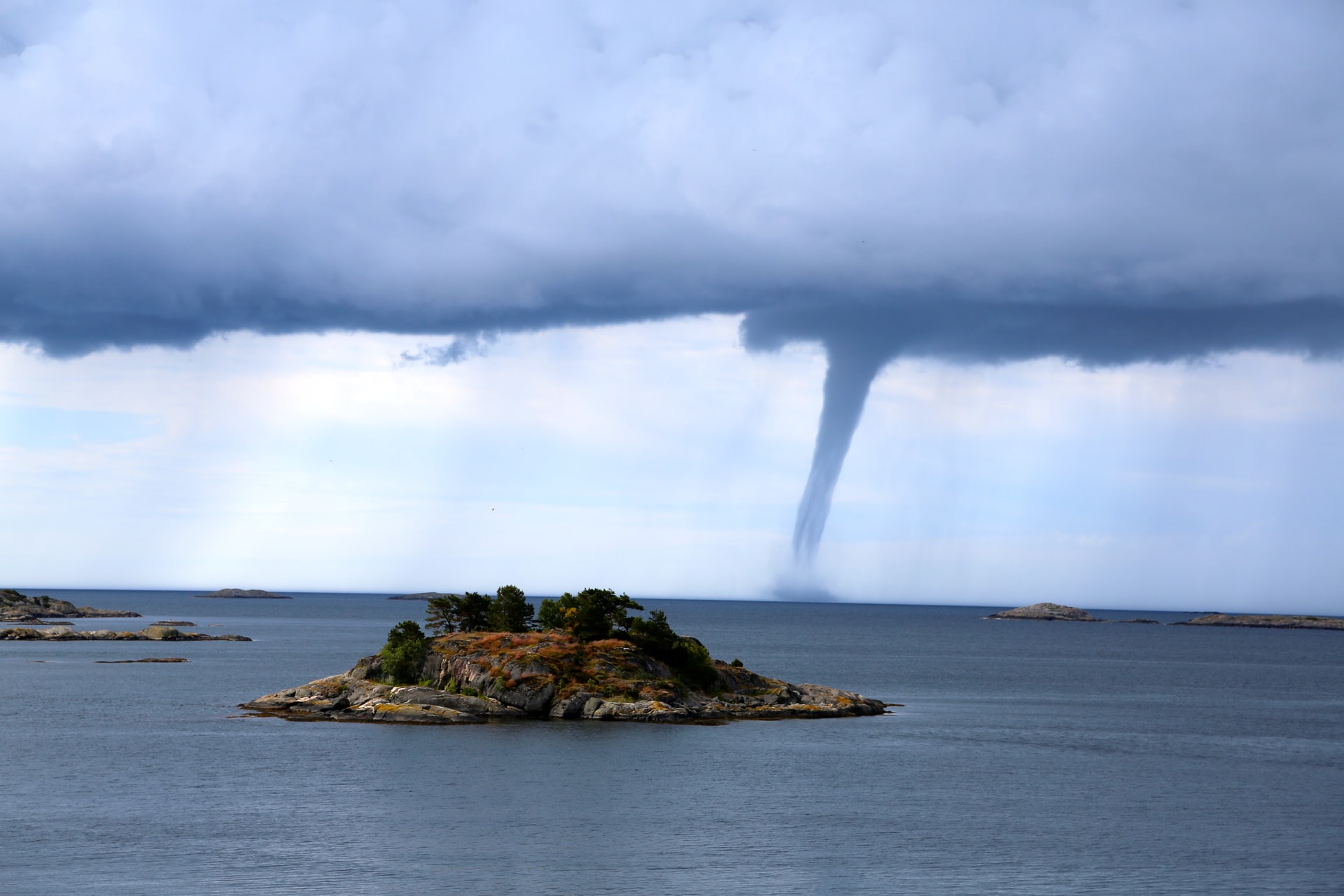 A photo of a tornado getting near a small island covered with trees