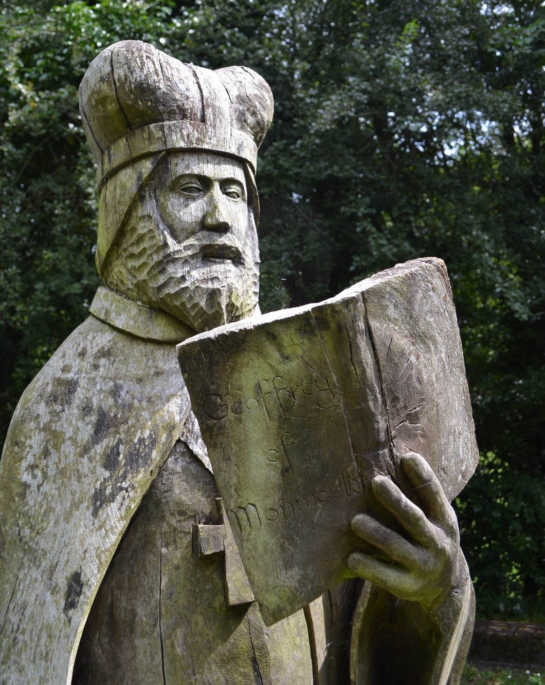Photograph of a statue of Geoffrey of Monmouth at Tintern Station. Statue is a wooden sculpture of a figure in bishop's garb, holding a book with 