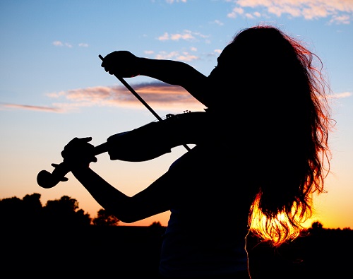 Woman silhouette playing violin in sunset light with hair highlighted