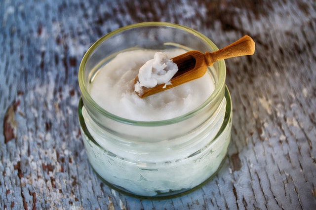 Open jar of white substance like coconut oil. It has a small, wooden scoop, which has a bit of the sunstance on it
