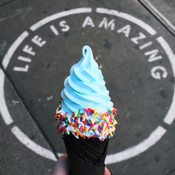 A blue soft icecream cold held above a sign on the ground reading Life is Amazing.