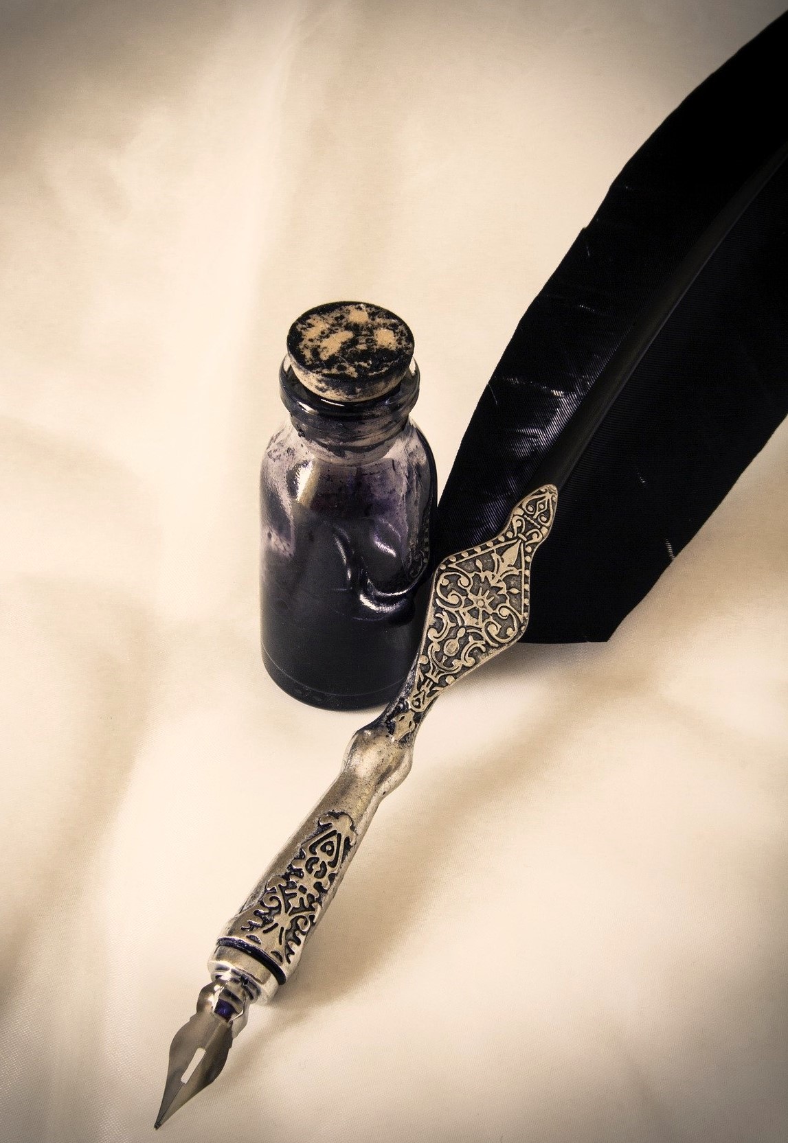 Quill with raven feather and ornate silver nib next to a small vial of ink
