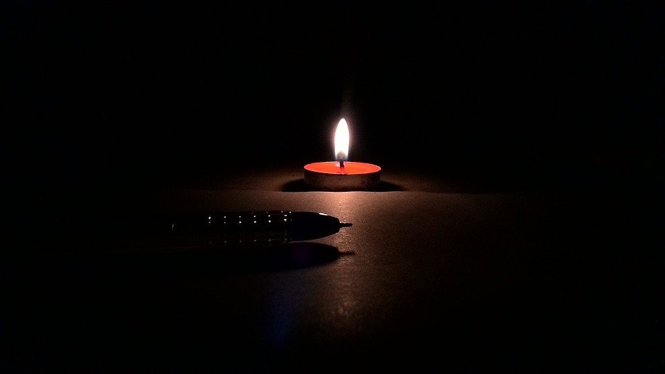 A pen lying on a table in darkness, backlit by a tea light candle