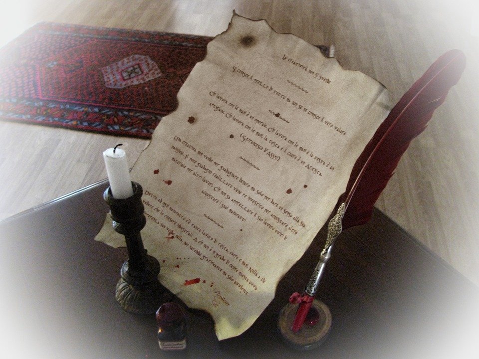An old parchment document on a stand, surrounded by quill pen and candle